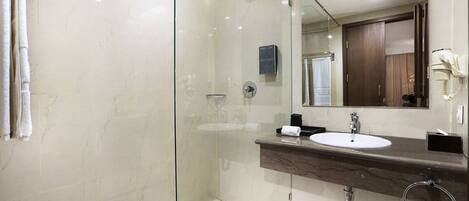 Un baño moderno con ducha envuelta en vidrio, pared con mosaicos de mármol, lavamanos con encimera oscura y espejo con marco de madera.