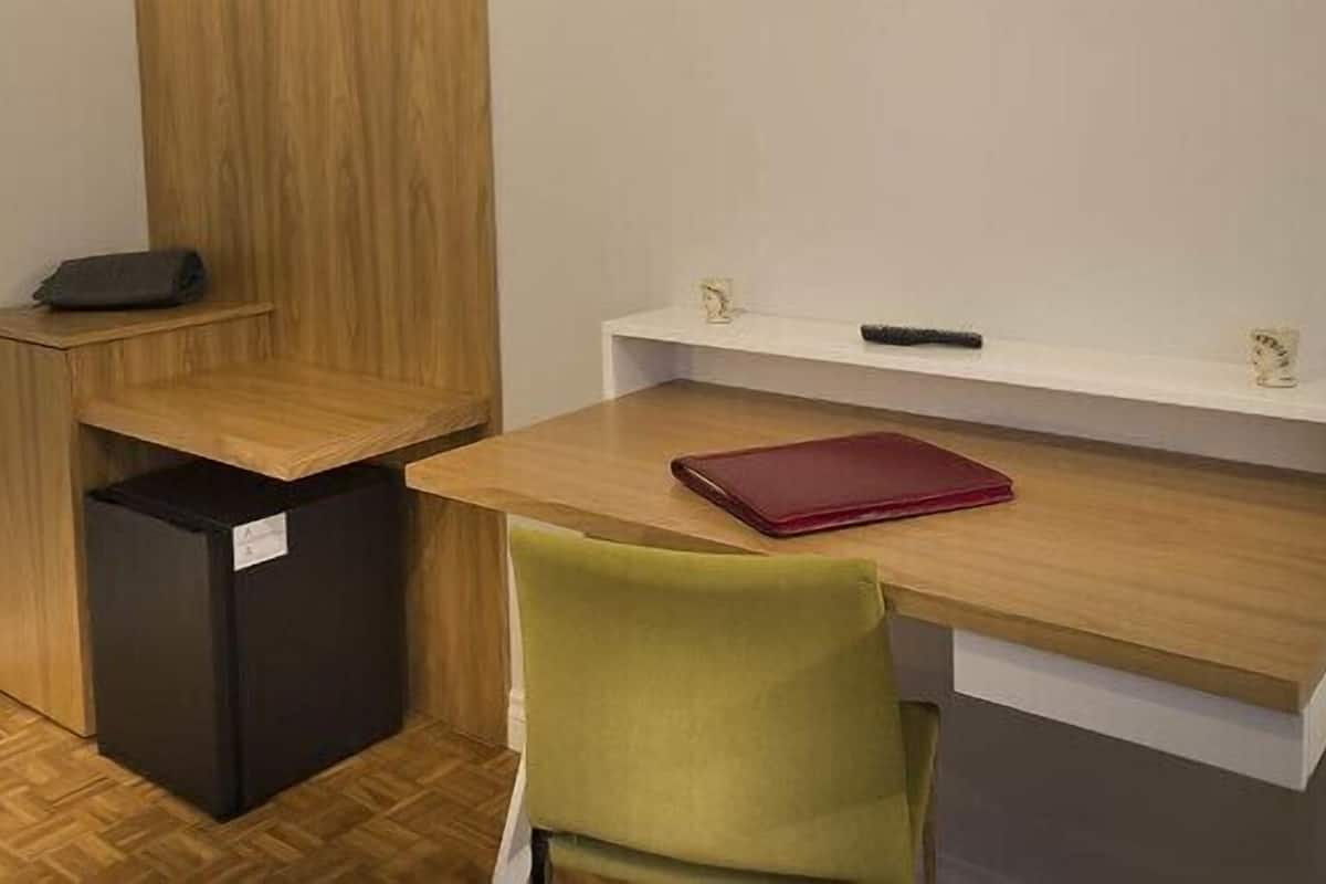 Une pièce de taille modeste, avec un bureau en bois, un petit réfrigérateur noir et une chaise verte.