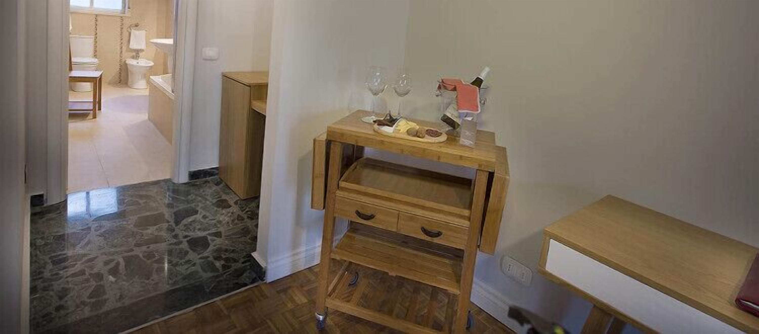 Ein Holztisch mit einer Weinflasche und Gläsern, ein Fliesenboden aus Stein und ein hölzerner Stuhl in einem Zimmer mit weißen Wänden.