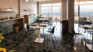 A modern dining area with marble flooring, multiple tables and chairs, and a view of the sea through large windows. - Ciauru Design B&B (Messina)