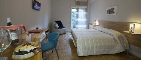 Habitación de hotel con cama, escritorio con silla, televisión y ventana con vista a zonas verdes.