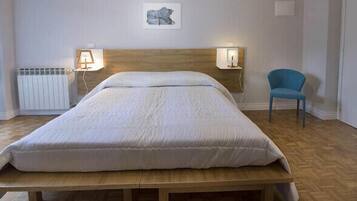 A bedroom with a wooden headboard, a bed with white bedding, two bedside lamps, a radiator, a chair, and a wall-mounted artwork.