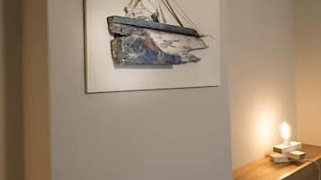 A wall-mounted abstract painting with a textured surface and a small table with a light on it.