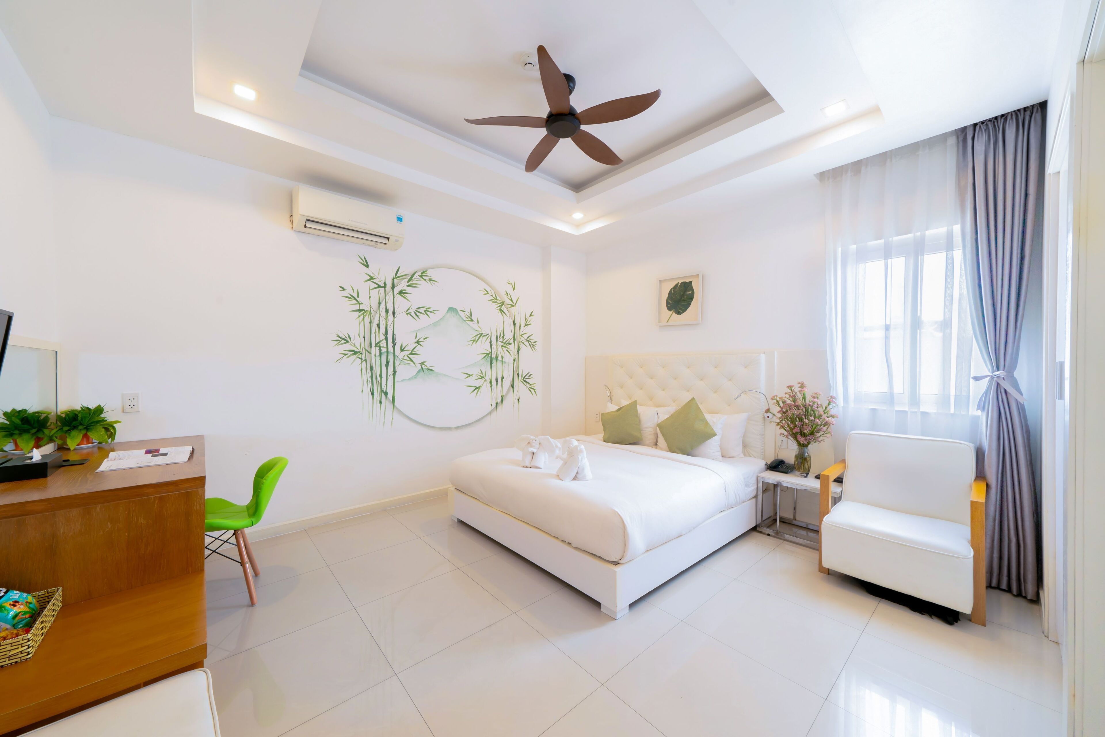 A modern hotel room with a bed, a desk, a chair, a ceiling fan, and a window with curtains.