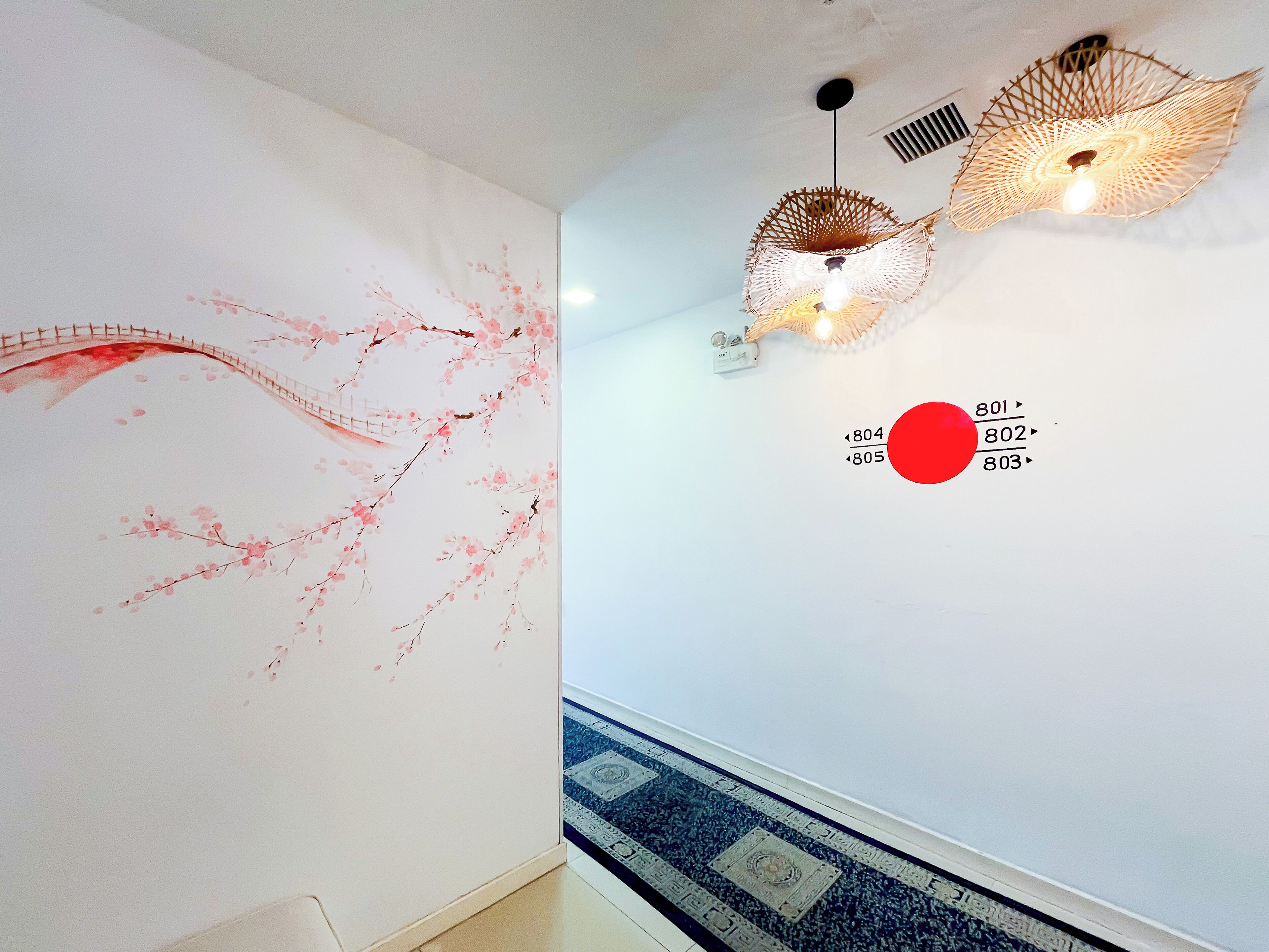 Un pasillo con un mural de cerezos en flor, una lámpara decorativa colgante y una alfombra estampada.