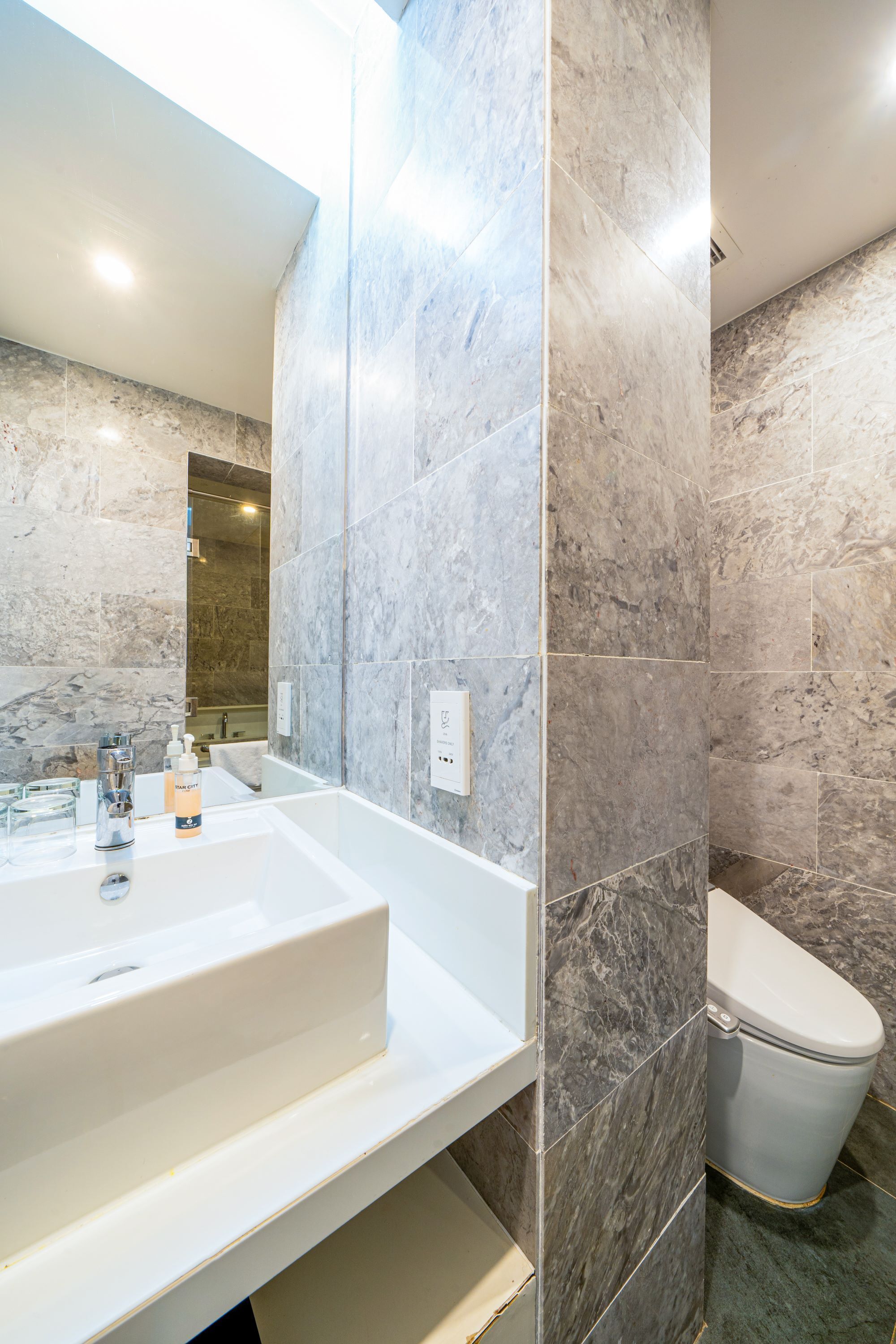 Une salle de bain moderne avec un lavabo blanc, un grand miroir et des toilettes.