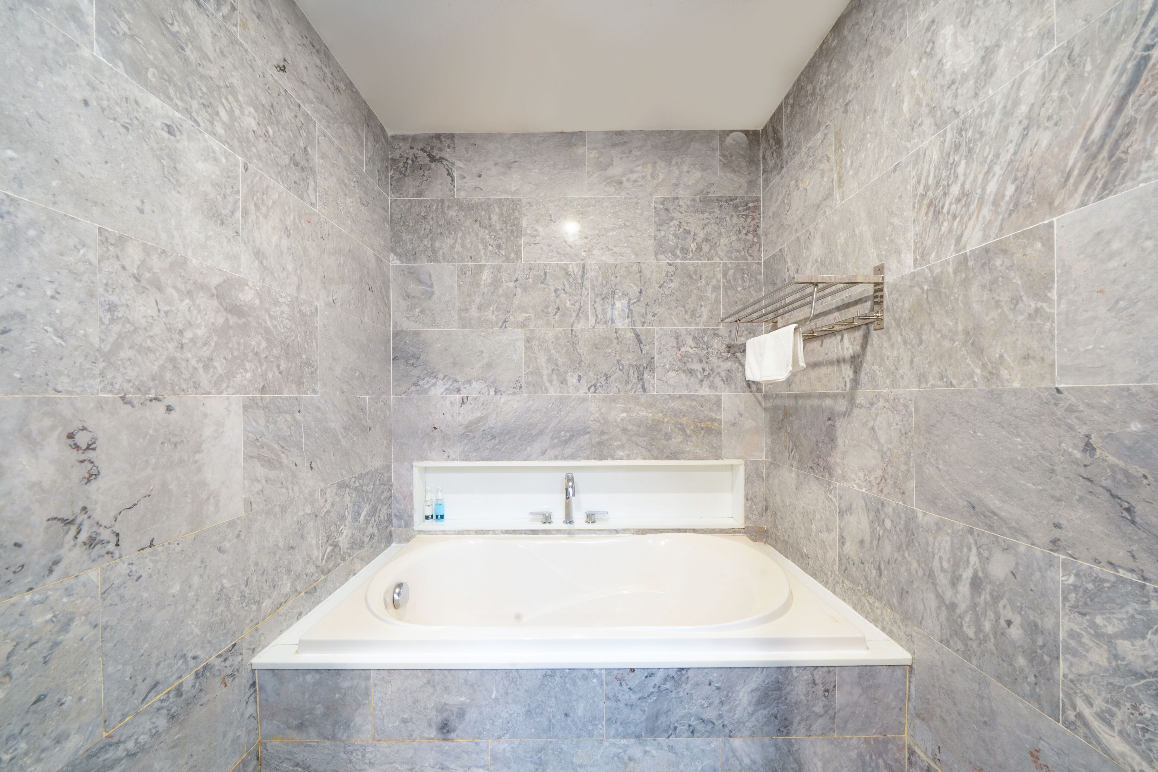 A modern bathroom with a freestanding bathtub, marble walls, and a towel rack.