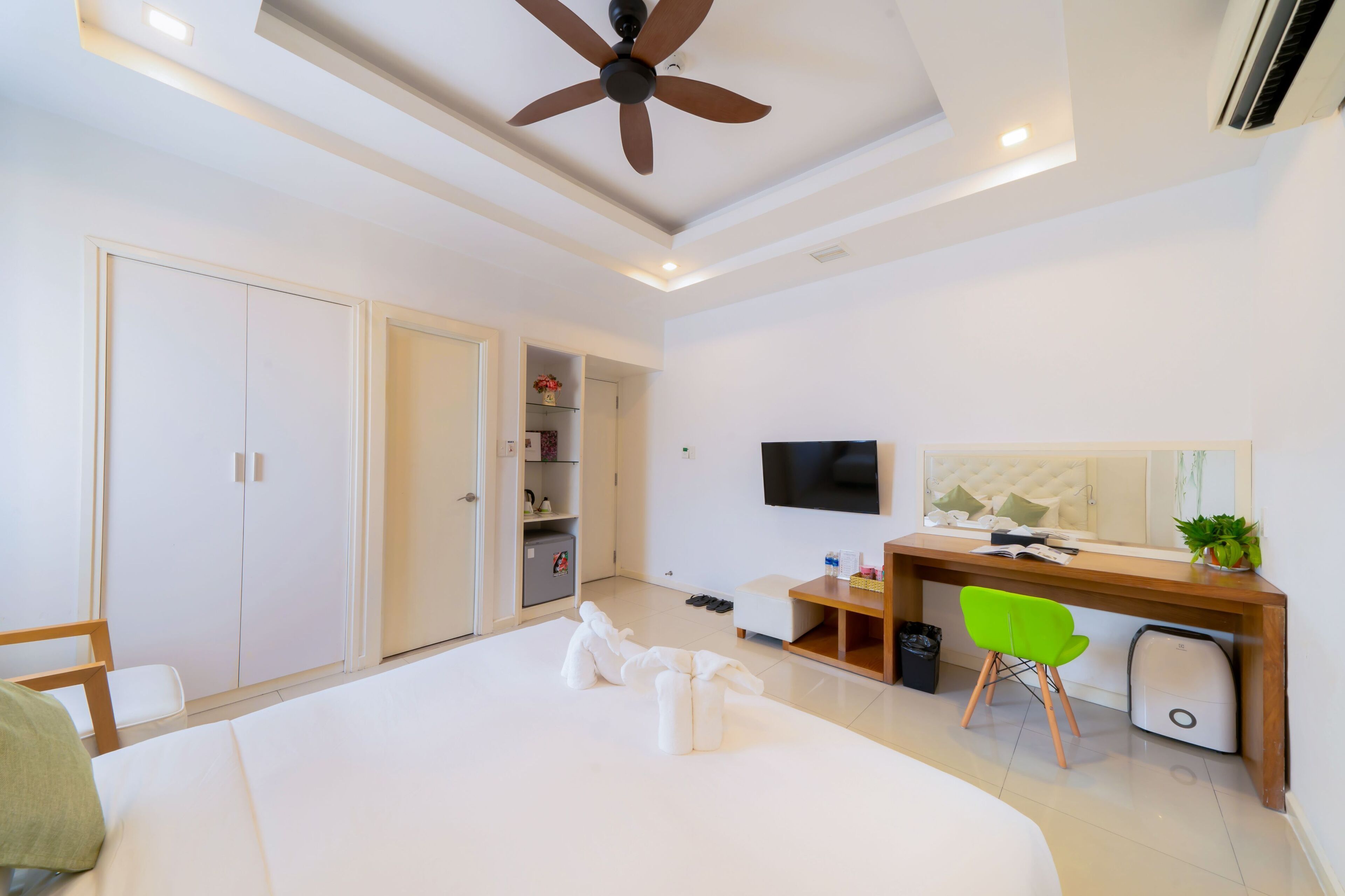 A modern hotel room with a large bed, a desk with a chair, a TV, and a ceiling fan.