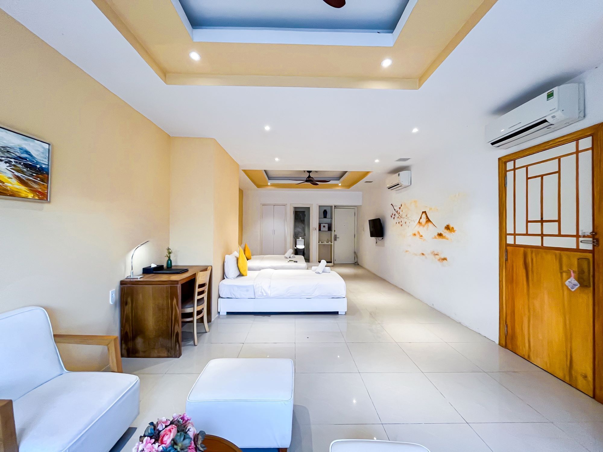 A hotel room with a bed, a desk, a chair, a sofa, a small table with flowers, and a wardrobe.
