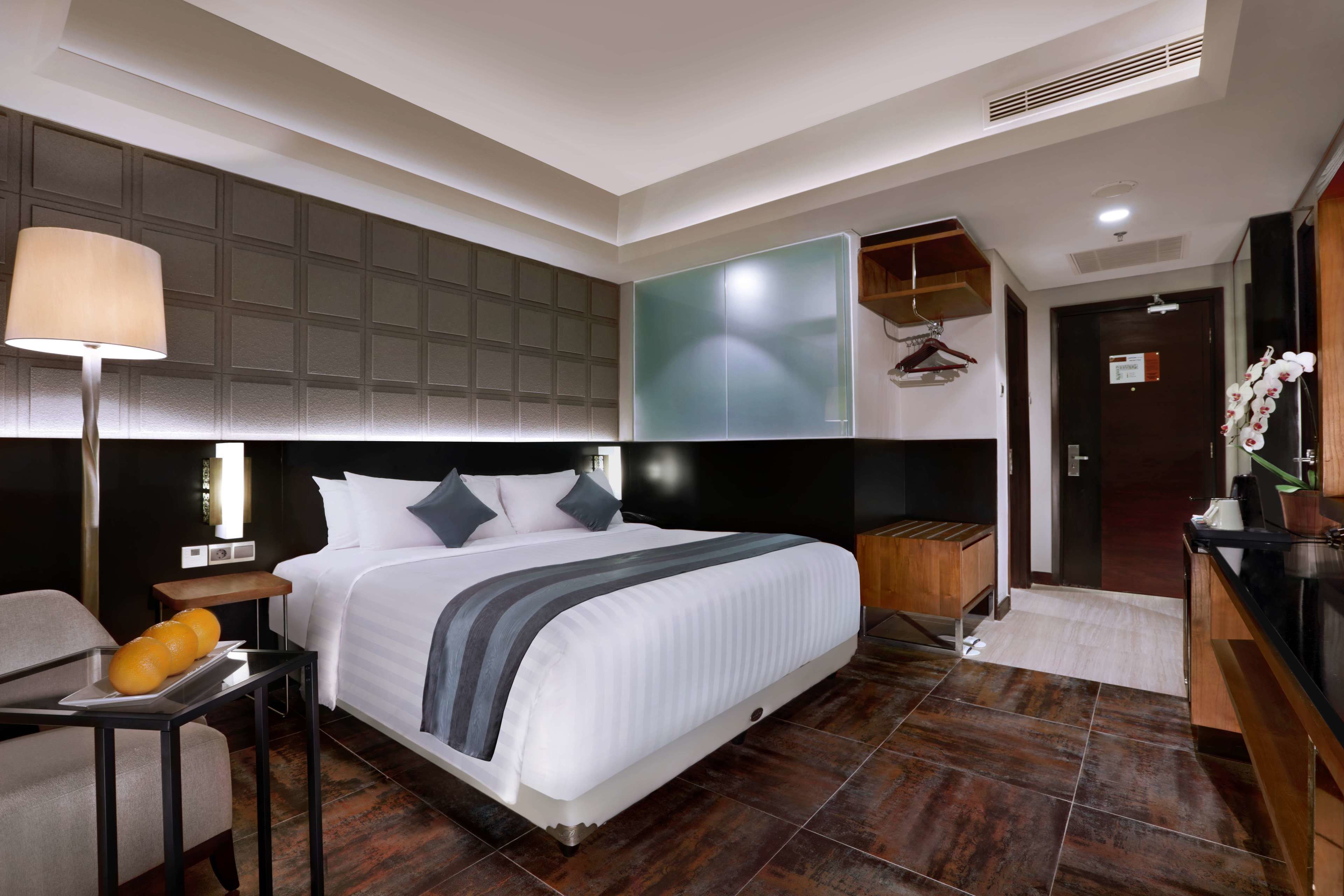 Ein modernes Hotelzimmer mit einem großen Bett, einem Schreibtisch mit Lampe, einem Holztischchen und einem Badebereich mit Dusche und Toilette.