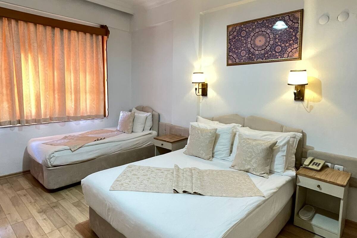Habitación de hotel con dos camas, un ventanal con cortinas, una obra de arte colgada en la pared y una mesita de noche con lámpara.