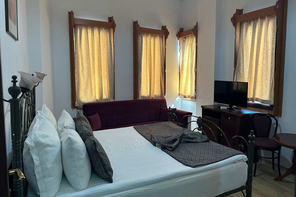 Una habitación de hotel con cama, escritorio, silla, televisión y cortinas en las ventanas.