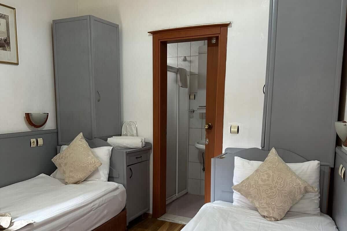A hotel room with two beds, a wardrobe, a bathroom visible through a door, and an air conditioning unit on the wall.