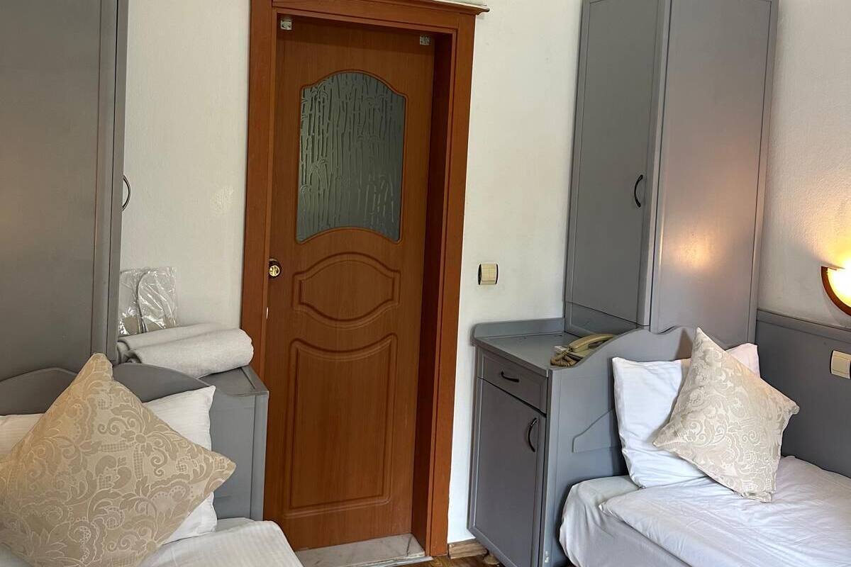 Una habitación de hotel con dos camas, una puerta de madera, un armario, una mesita de noche y un equipo de aire acondicionado.