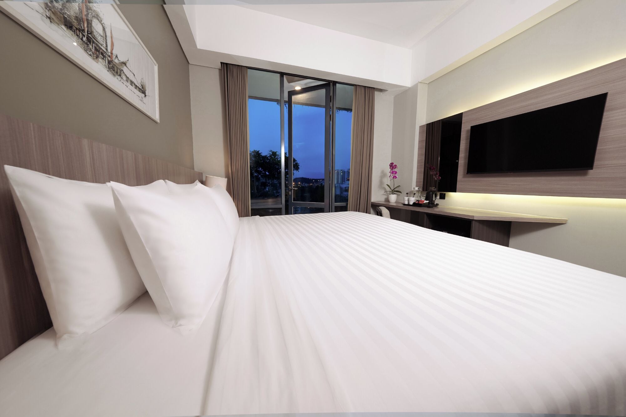 Ein Hotelzimmer mit einem großen Bett, einem an der Wand montierten Fernseher und Blick auf die Stadt.