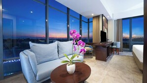A modern hotel room with a large window, a sofa, a desk, a chair, and a bed. - Aston Inn Mataram (Mataram)