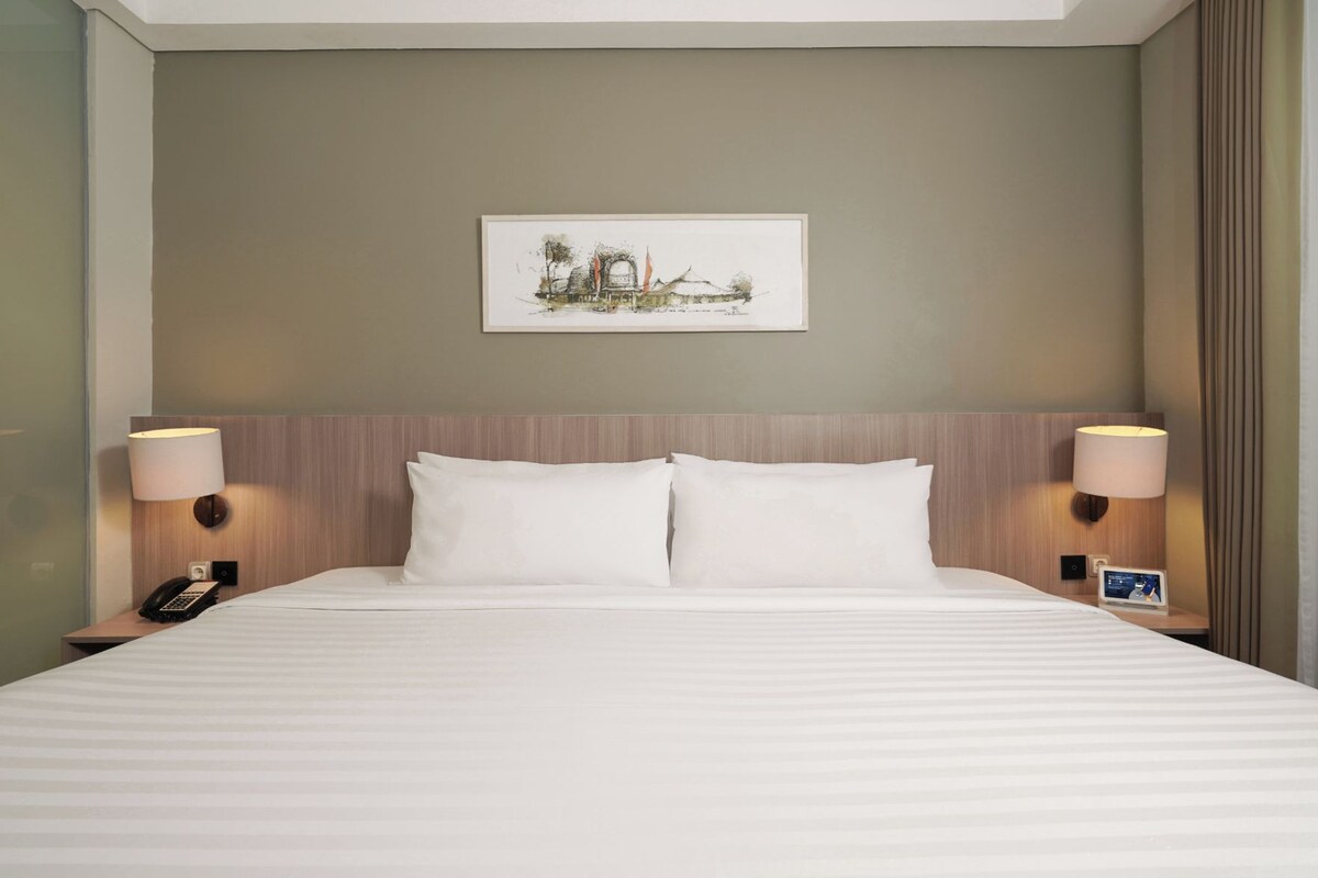 A hotel room with a large bed, two bedside lamps, a nightstand with a phone, and a framed picture on the wall.