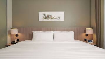Una habitación de hotel con una cama grande, dos lámparas de noche, una mesita de noche con un teléfono y un cuadro en la pared.