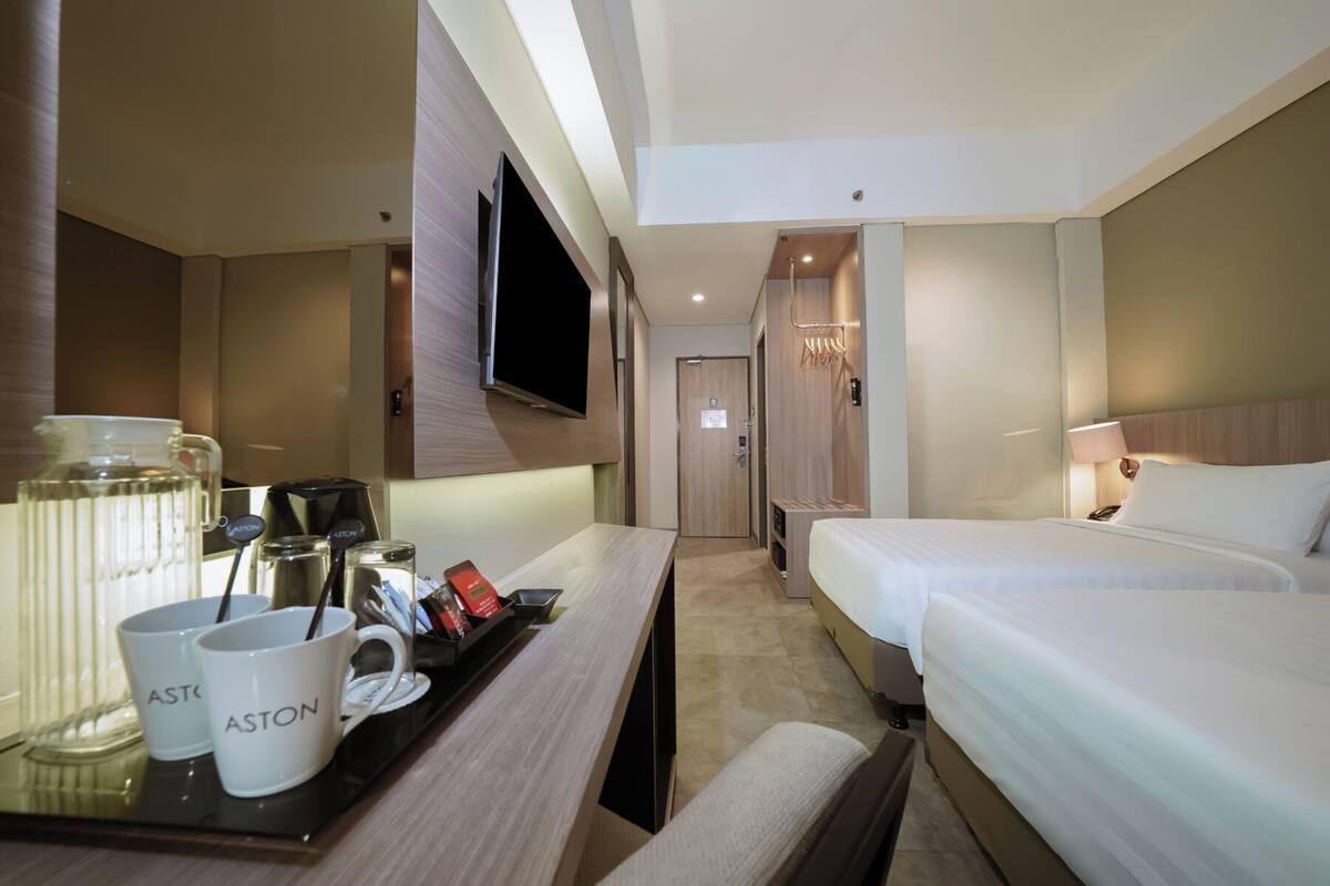 A hotel room with a bed, a TV, a desk with a coffee maker, and a minibar.