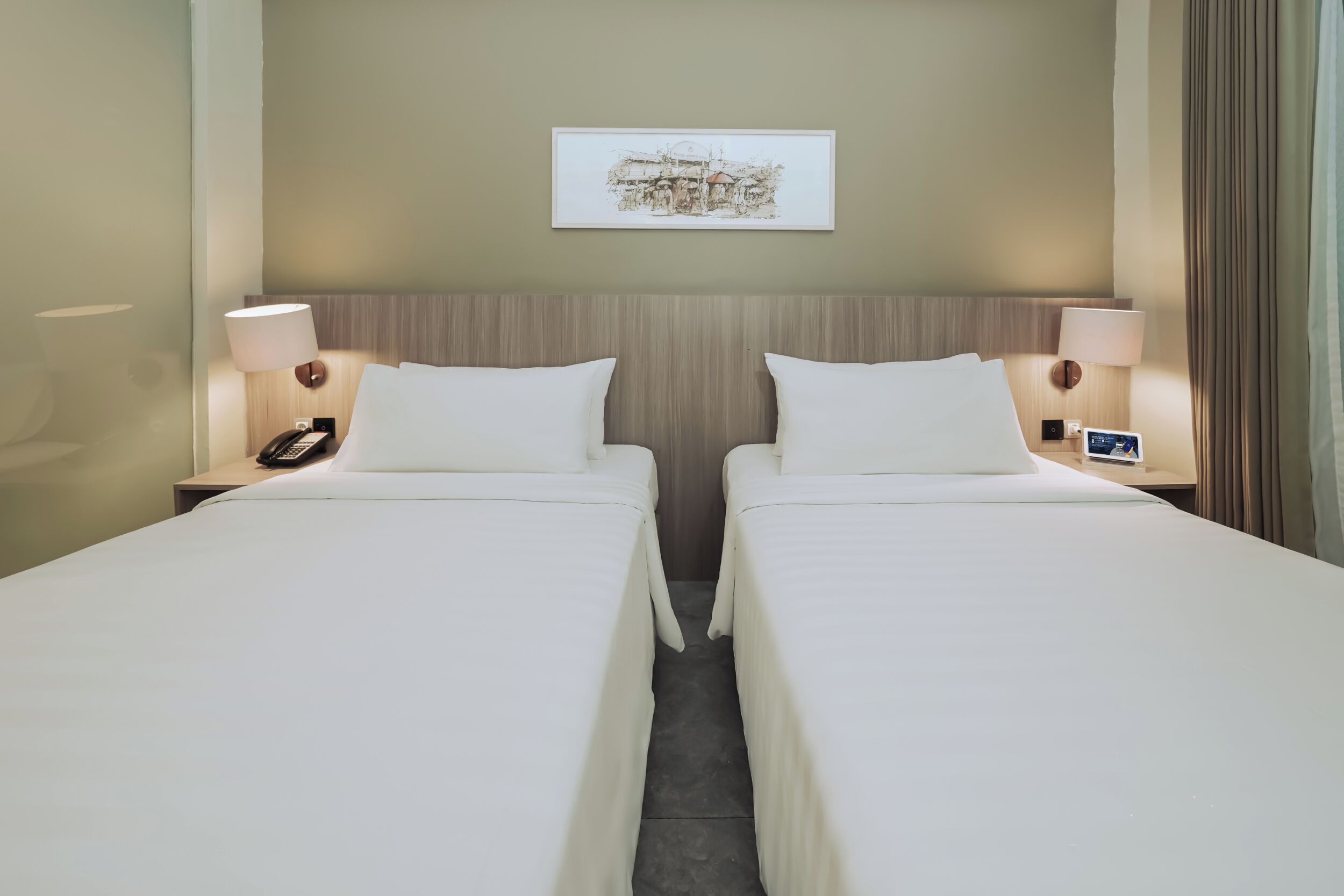 A hotel room with two single beds, a bedside phone, a small table, a lamp, and a framed picture on the wall.