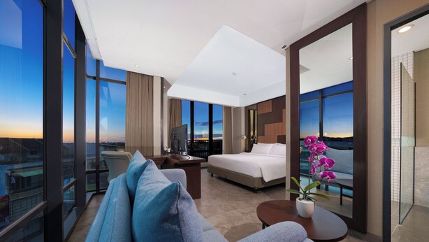 A modern hotel room with a large bed, a sofa, a desk, and a view of the cityscape. - Aston Inn Mataram (Mataram)