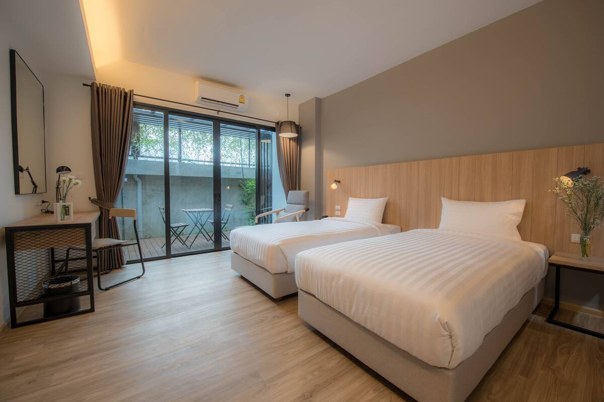 A modern hotel room with two beds, a desk, and a balcony with a view.
