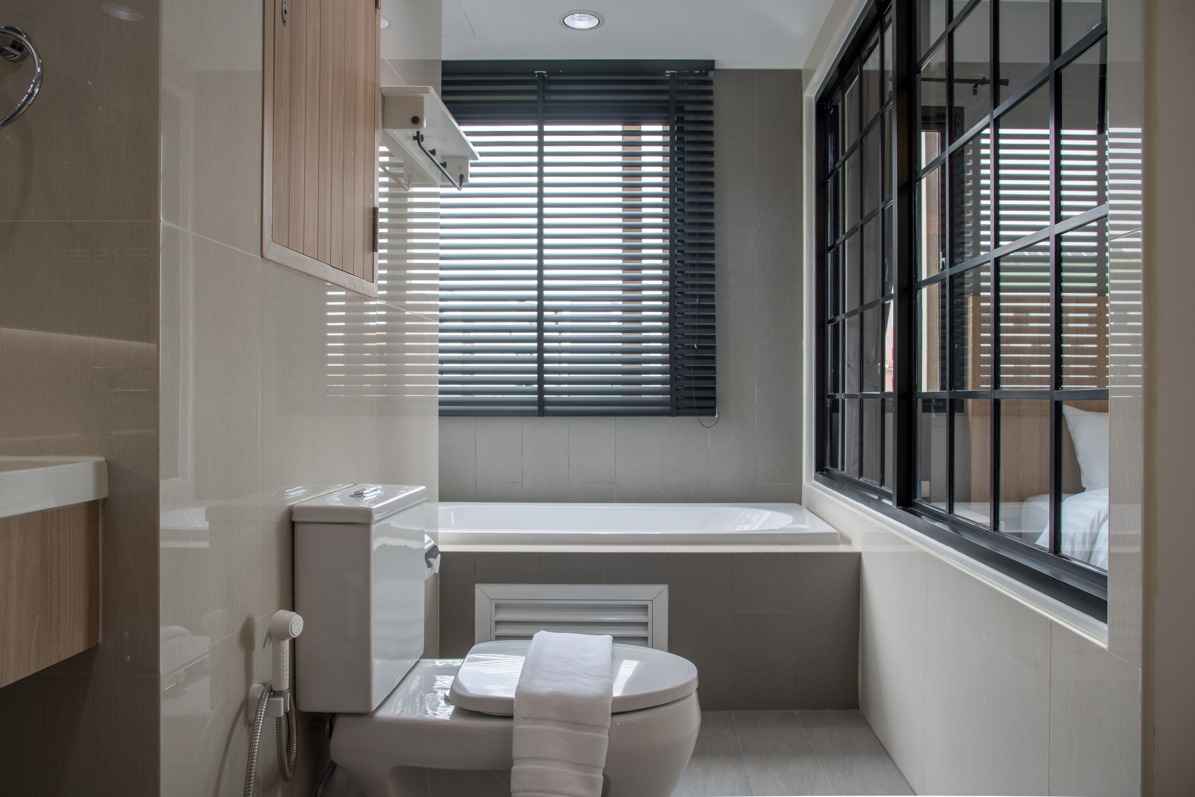 Une salle de bain moderne avec une baignoire, des toilettes et une fenêtre équipée de stores.