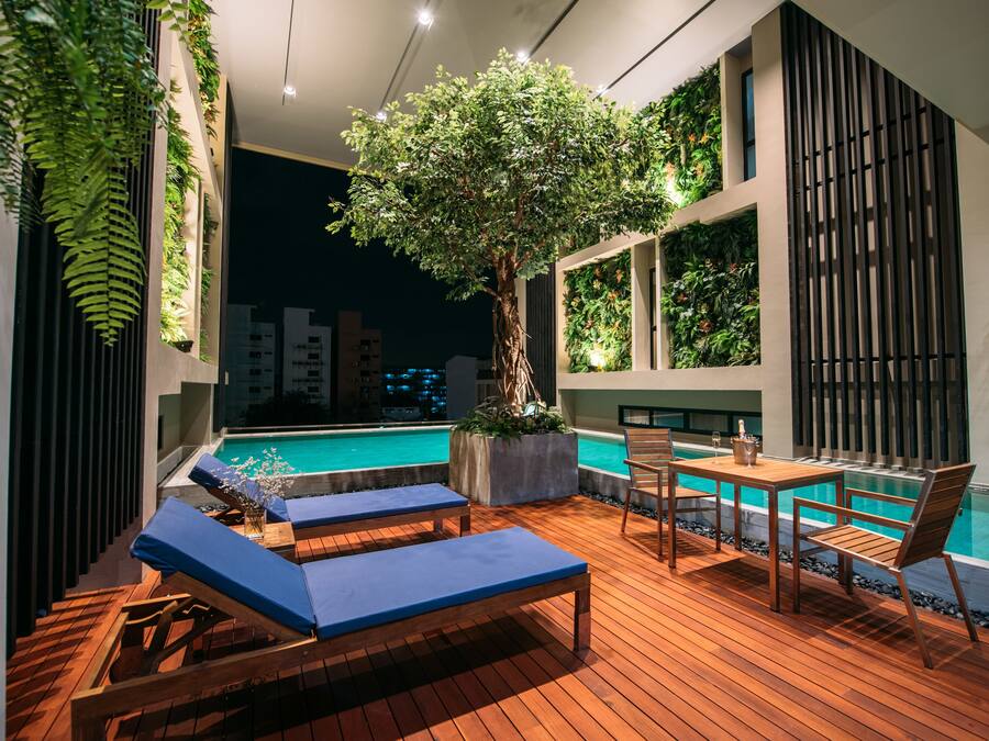 A rooftop pool area with lounge chairs, a wooden table, and a potted tree.