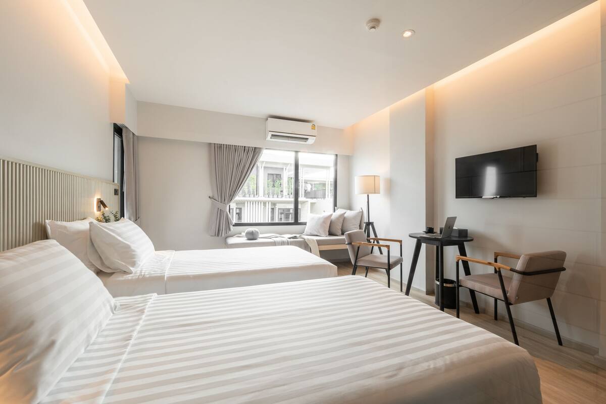 A hotel room with two beds, a TV, a desk with a chair, and a view of the outdoors.