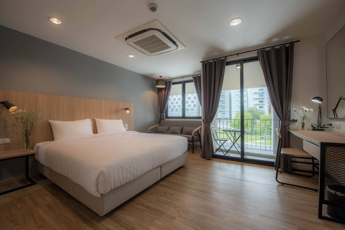 A modern hotel room with a large bed, a desk, and a balcony with a view of the city.