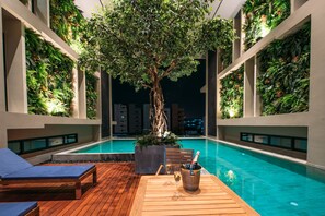 A poolside area with a wooden deck, lounge chairs, a table with a bottle and glass, and a tree planter. - Mii Hotel Srinakarin (Bangkok)