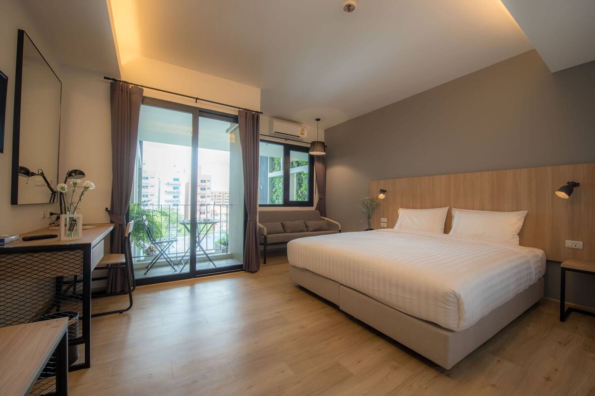 A modern hotel room with a large bed, a desk, and a balcony with a view of the city.