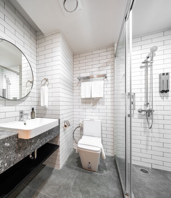 A modern bathroom with white subway tiles, a granite countertop sink, a toilet, and a glass-enclosed shower area. - Mii Hotel Srinakarin (Bangkok)