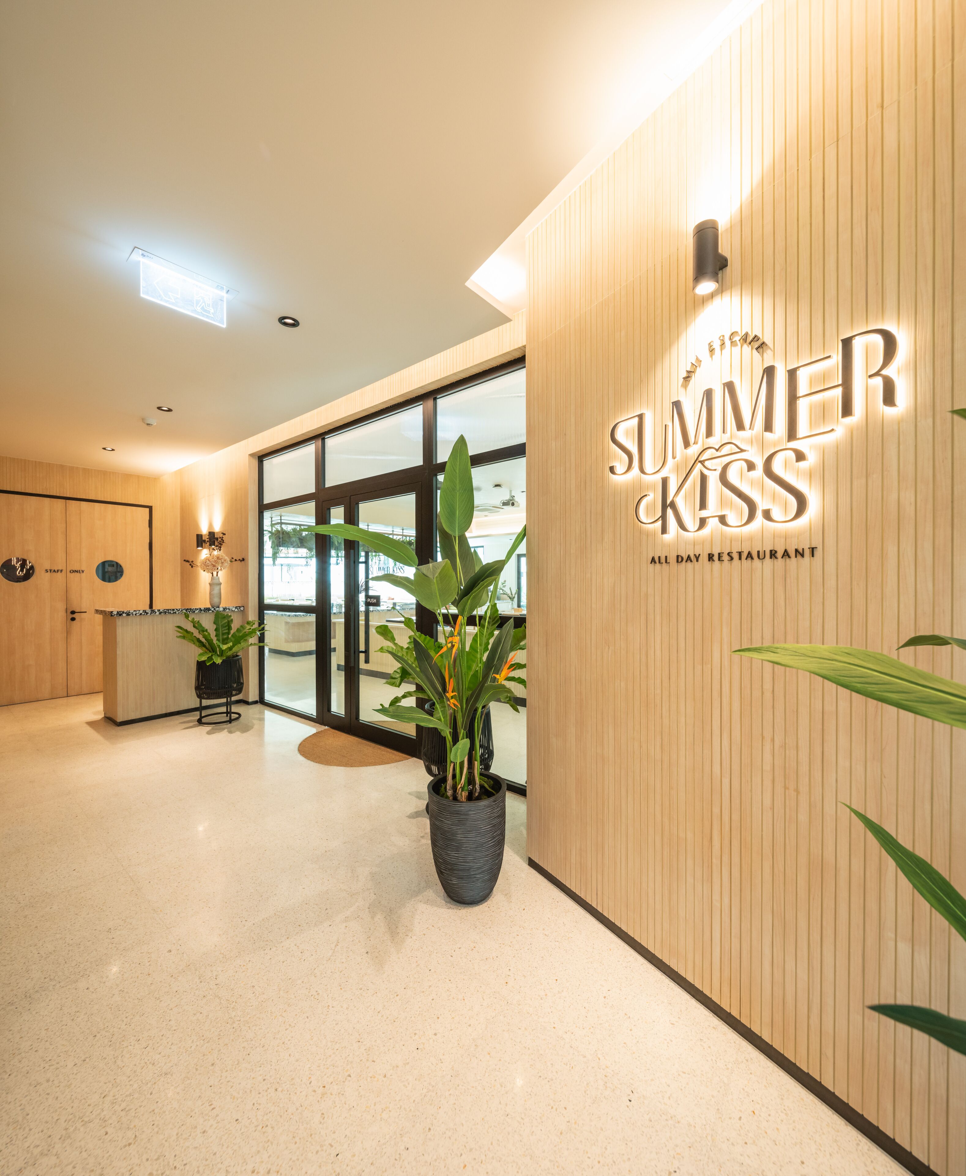 A modern interior with a wooden wall, a large potted plant, and a sign reading "SUMMER KISS ALL DAY RESTAURANT".