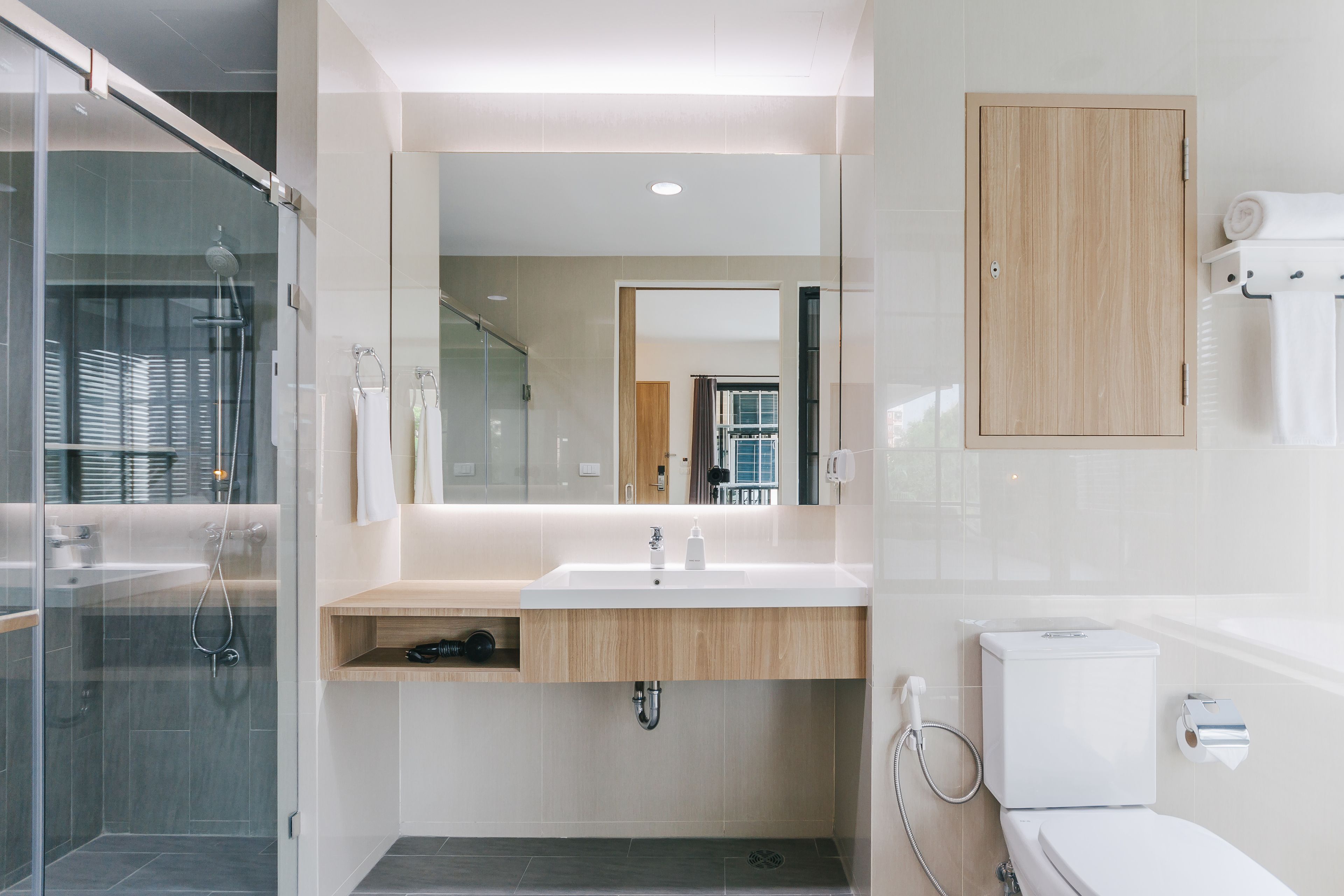 A modern bathroom with a glass shower enclosure, a wooden vanity, a large mirror, and a toilet.