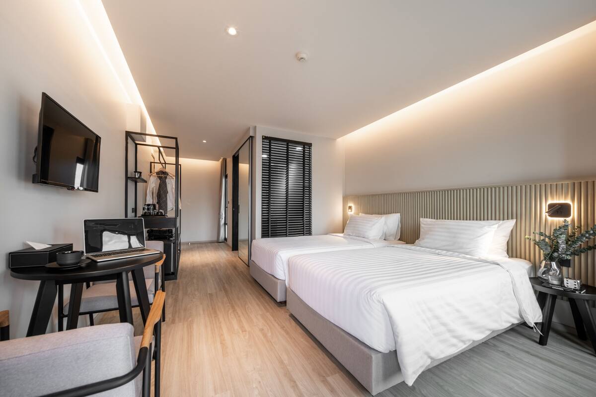 A modern hotel room with a large bed, a desk with a laptop, a TV, and a mirror.