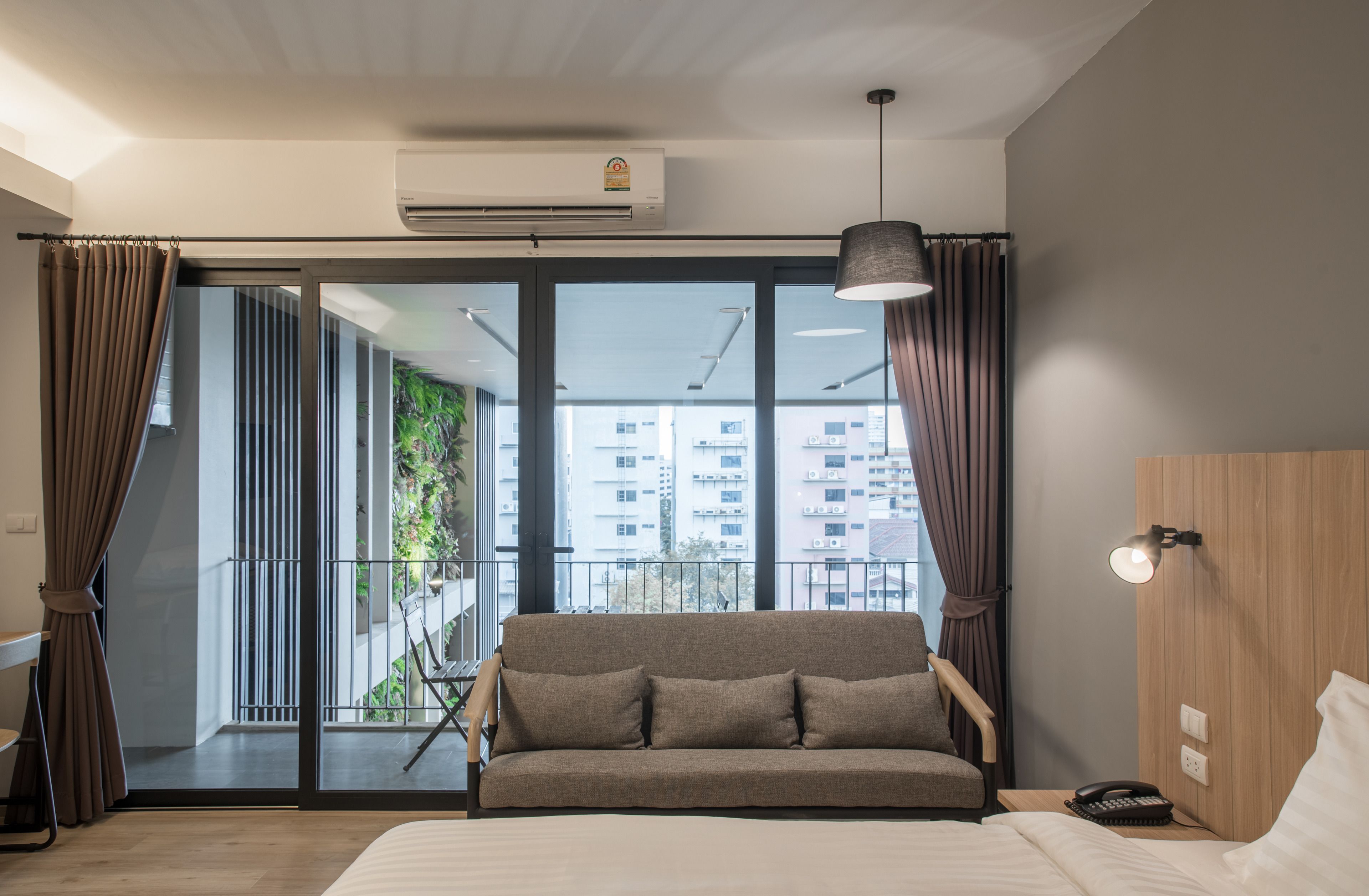 A modern hotel room with a large bed, a sofa, a desk, and a view of a balcony with a cityscape.