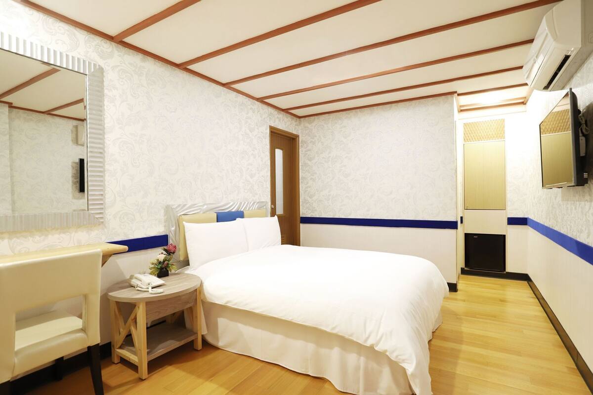 A hotel room with a bed, bedside table, chair, and a mirror.