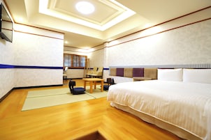 Una habitación de hotel con una cama grande, piso de madera, una mesita y sillas.