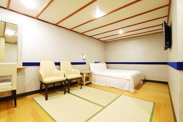 A hotel room with a bed, two chairs, a small table, a mirror, and a TV mounted on the wall.