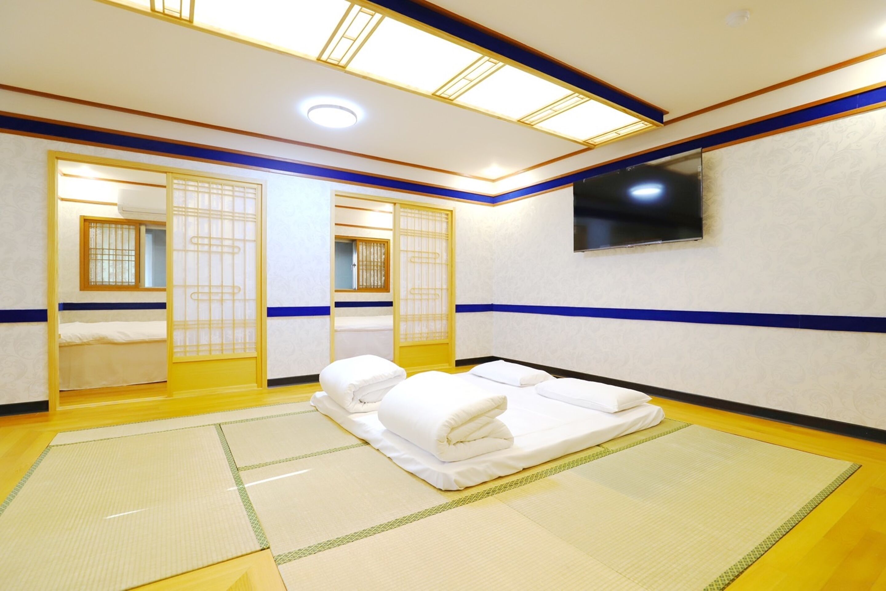 A traditional Japanese room with tatami flooring, a futon bed, sliding doors, and a television on the wall.