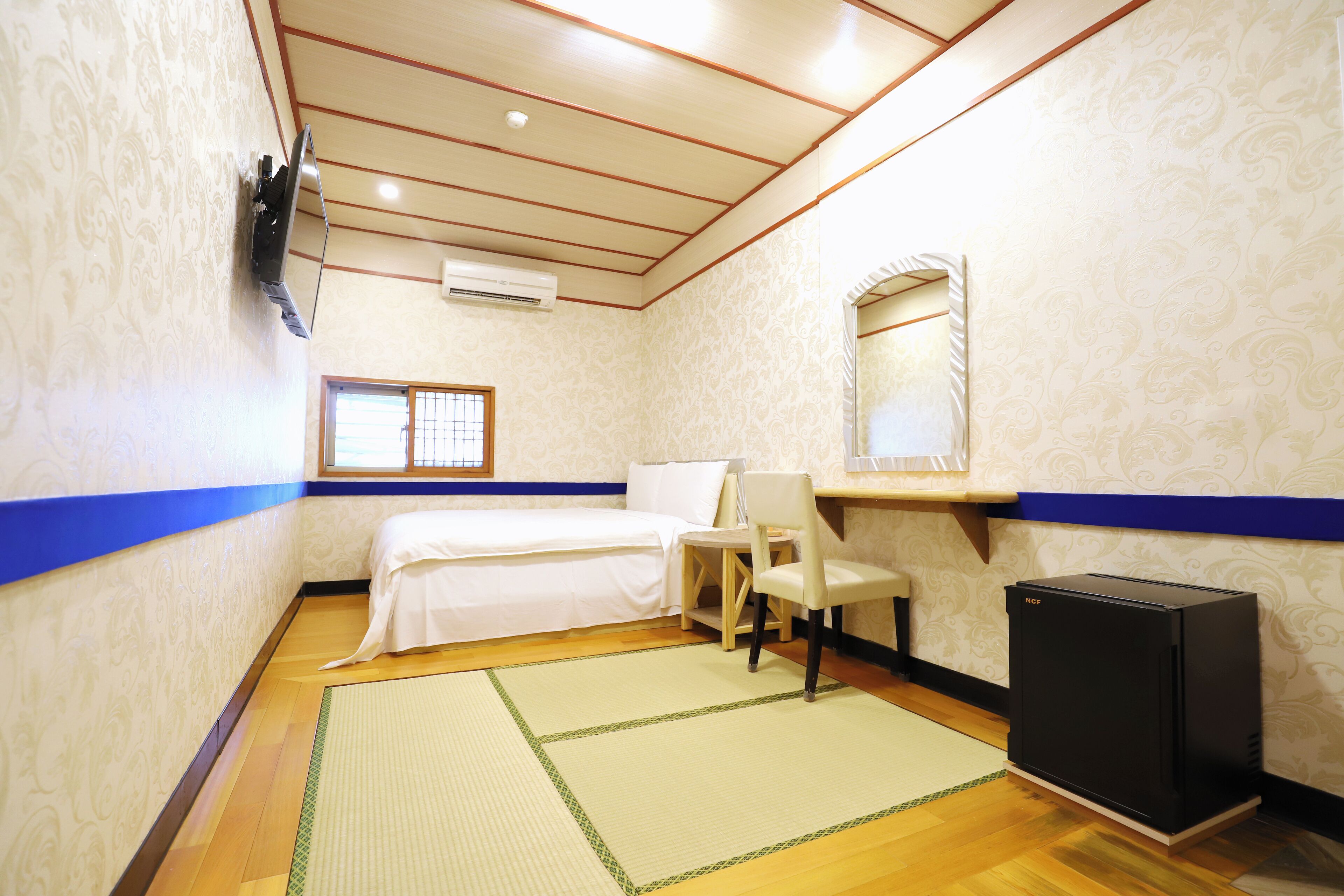 Une chambre d’hôtel avec un lit, une chaise, une petite table, un téléviseur et un radiateur.