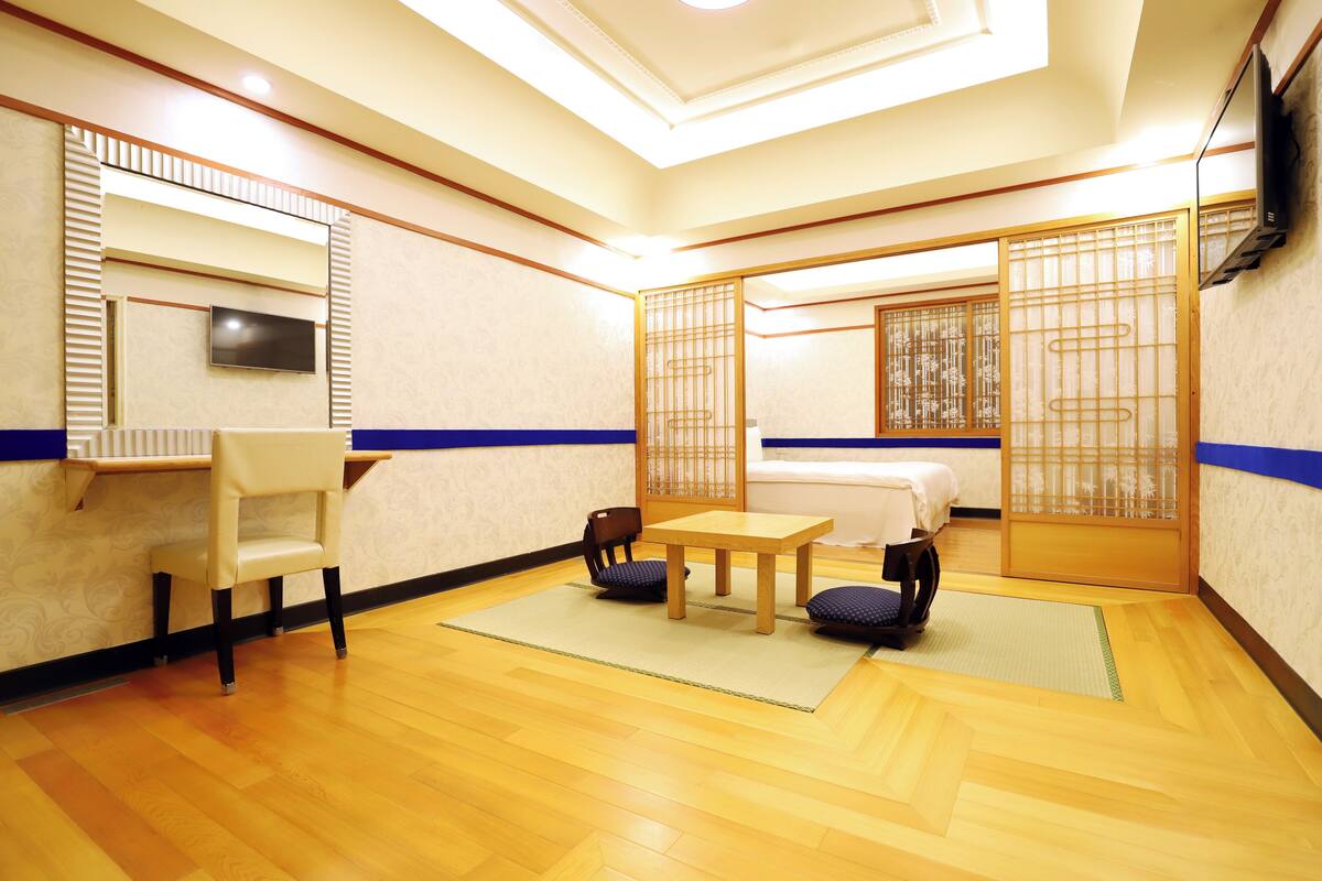 A traditional Japanese-style room with tatami flooring, a low table with cushions, a television mounted on the wall, and sliding doors.