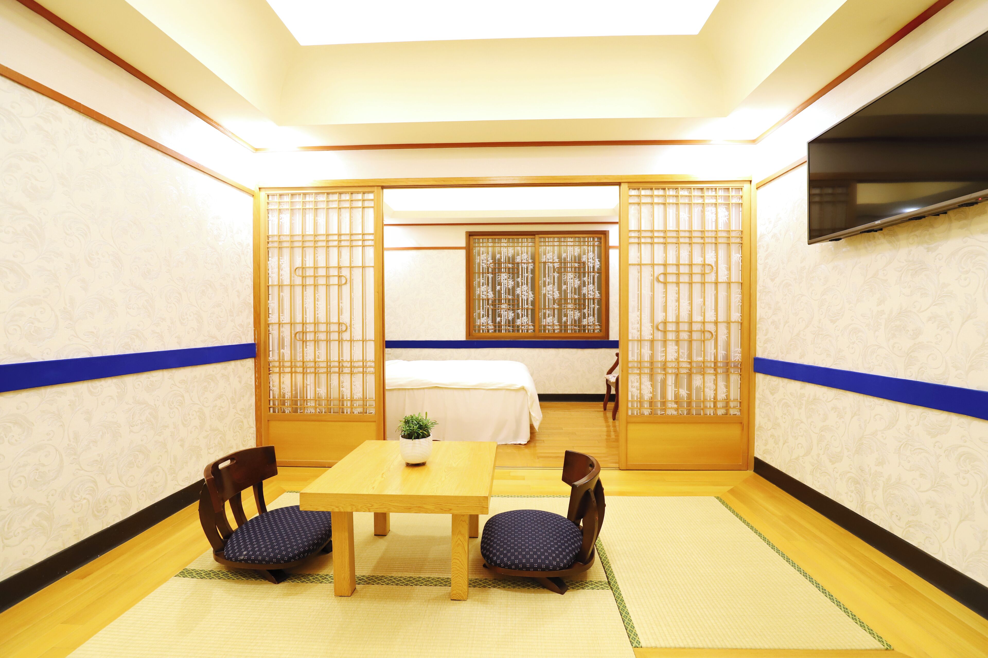 Et traditionelt japansk værelse med tatamimåtter, et lavt bord, to stole, en seng med hvid dyne og skydedøre med bambusmønster.