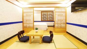 Et traditionelt japansk værelse med tatamimåtter, et lavt bord, to stole, en seng med hvid dyne og skydedøre med bambusmønster.