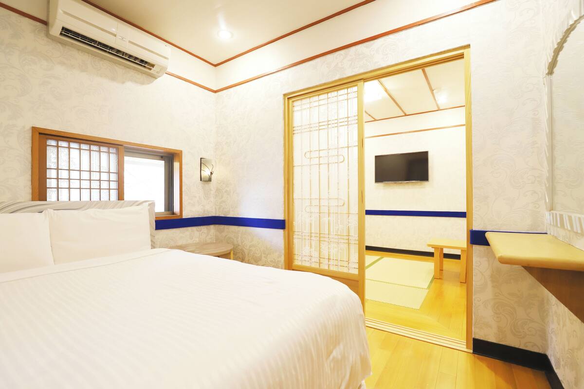 A hotel room with a bed, a TV mounted on the wall, a sliding door, and a small bench.