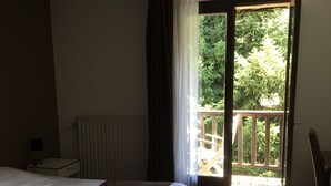 A bedroom with a bed, a radiator, a nightstand, and a view of a balcony with a wooden railing. - Auberge de Violaine (Monetier-les-Bains)