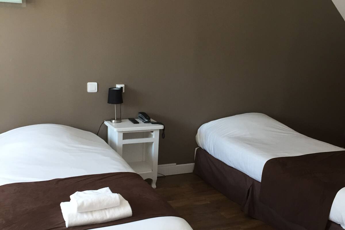 A hotel room with two beds, a nightstand with a lamp, and a phone.