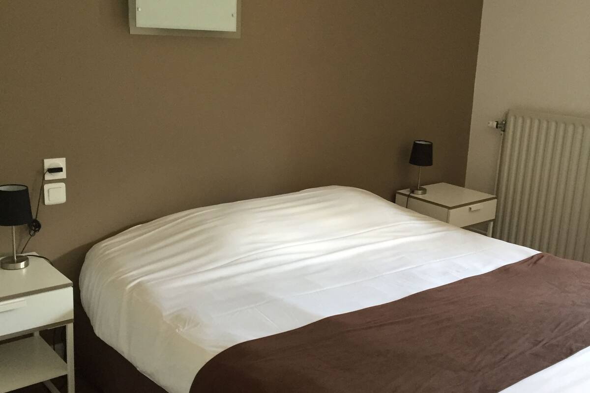 A hotel room with a bed, a nightstand, a lamp, and a radiator.