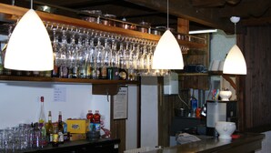 A bar area with multiple hanging light fixtures, shelves stocked with glassware, and various bottles and cans on the counter. - Auberge de Violaine (Monetier-les-Bains)
